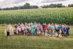Group of people posing for photo in front of corn field.