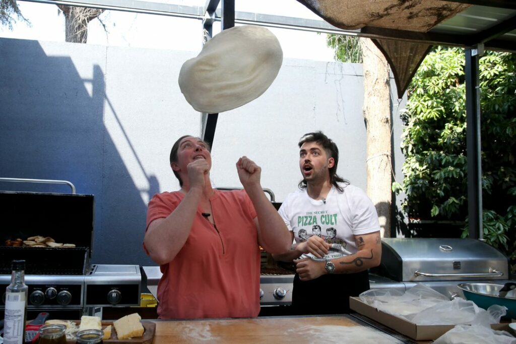 Woman tosses pizza crust in air as a man watches on.